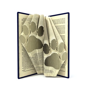 May include: A book with pages folded into the shape of two paw prints. The book is open and the pages are folded to create a 3D effect. The book is blue and the pages are white.