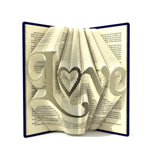 May include: A book with the word "Love" folded into the pages. The book is open and the pages are folded to create the word. The book is on a white background.