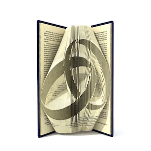 May include: A book with pages folded into a three-dimensional design, creating a complex geometric shape. The book is open and the folded pages are visible, creating a unique and intricate artwork.