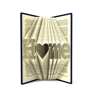Könnte beinhalten: Ein Buch mit den Worten "Ich liebe Zuhause" in die Seiten gefaltet. Das Buch ist geöffnet und die Seiten sind gefaltet, um die Worte und eine Herzform zu bilden.
