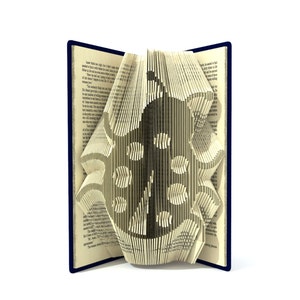 Könnte beinhalten: Ein Buch mit Seiten, die zu einem dreidimensionalen Design eines stilisierten Friedenssymbols gefaltet sind. Das Buch ist geöffnet und die Seiten sind gefaltet, um ein erhabenes Design zu schaffen. Das Buch ist außen blau und die Seiten sind cremefarben.