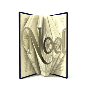 May include: A book with pages folded to create the word "Noel" in a 3D design. The book has a blue cover.