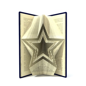 May include: A book with pages folded into a 3D star shape. The book is open and the star is visible. The book has a blue cover.