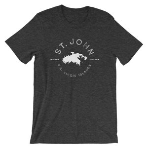May include: Dark grey t-shirt with a white graphic of the island of St. John, US Virgin Islands, with the text "ST. JOHN" and coordinates "18.181644°N 64.973289°W".