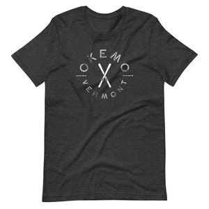 May include: A dark heather grey t-shirt with a white graphic of crossed skis and the text "Okemo Vermont 43.9419°N 72.7419°W".