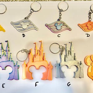 May include: Ten different keychains featuring various Disney characters and logos. The keychains are made of plastic and have a variety of colors, including yellow, silver, pink, orange, and purple. The keychains are all attached to silver key rings.