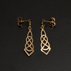 May include: A pair of gold-toned earrings with a Celtic knot design. The earrings are dangle style and have a teardrop shape.
