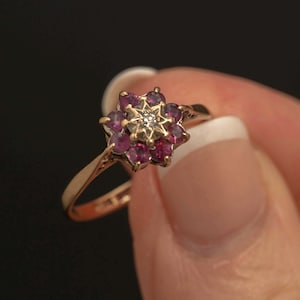 Peut inclure: Une bague en or ornée d'un motif floral avec un diamant central et des pierres rouges. Le design délicat de la bague est mis en valeur sur un fond sombre, soulignant son élégance et son savoir-faire.