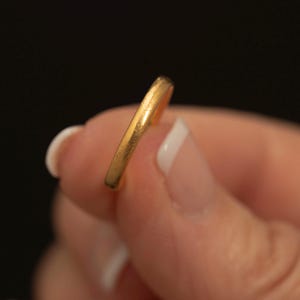 May include: A thin, circular gold ring with a smooth, matte finish. The band has a simple, rounded profile and a consistent yellow gold colour throughout its entire structure, showcasing a clean and unadorned design for a classic jewellery piece.