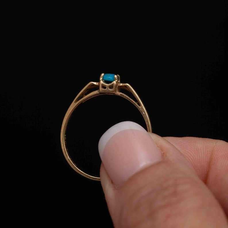 May include: A gold ring with a turquoise gemstone set in the center. The ring is simple and elegant.