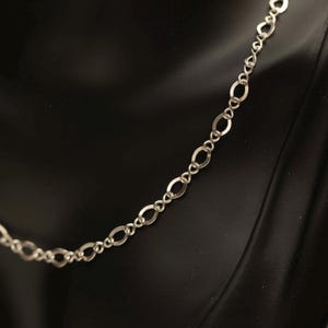 May include: A silver-toned chain necklace featuring a series of repeating oval-shaped links connected by smaller, twisted figure-eight style connectors. The metallic chain displays a polished finish and follows a consistent, repeating pattern throughout.