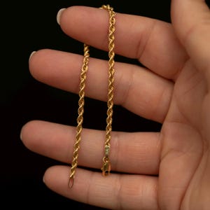May include: A gold rope chain necklace featuring a twisted metal link design. The chain includes a lobster claw clasp and a small metal tag near the closure that is clearly stamped with the word ITALY, indicating its origin and metal construction.