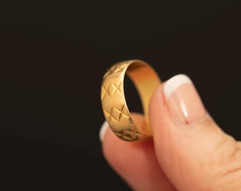 May include: A gold-toned band ring featuring a repeating embossed diamond pattern across its outer surface. The ring has a smooth, polished interior and a consistent width, showcasing a textured geometric design that wraps around the entire circumference.