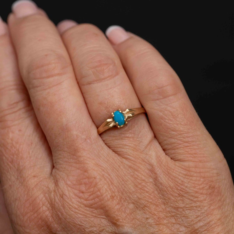 May include: A gold ring with a turquoise oval gemstone set in a simple, elegant design.