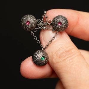 May include: A silver pendant with three round, textured charms. Each charm features a small, colourful gemstone in the centre. The pendant is attached to a silver chain.