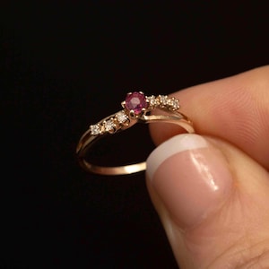 Peut inclure: Une délicate bague en or avec une seule pierre rouge et de plus petites pierres blanches serties dans une bande incurvée.