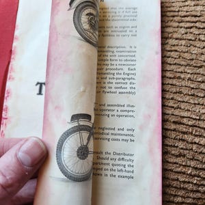 May include: Vintage book pages with illustrations of a motorcycle wheel. The pages are aged with a red border and text. The book is open, revealing the illustrations and text.