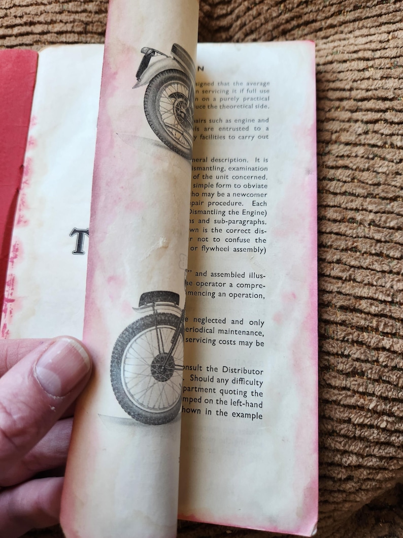 May include: Vintage book pages with illustrations of a motorcycle wheel. The pages are aged with a red border and text. The book is open, revealing the illustrations and text.