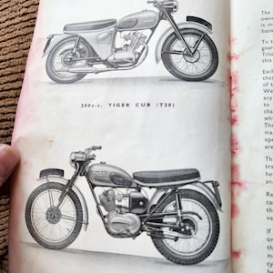 May include: Two vintage motorcycle illustrations from a book. The top image shows a motorcycle with a silver fuel tank and fenders, and the text "200c.c. TIGER CUB (T20)". The bottom image shows a similar motorcycle with the text "200c.c. TIGER CUB (T28C)".