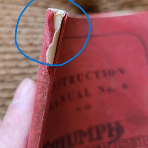 May include: Close-up of a vintage red instruction manual. The cover is worn, with visible wear and tear at the edges. The text "TRIUMPH TIGER CUB" is partially visible. The manual appears to be old and well-used.