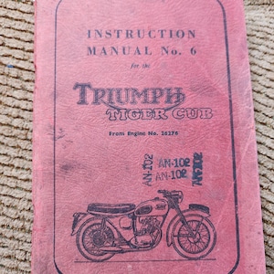 May include: A vintage Triumph Tiger Cub instruction manual. The cover is a faded red with black text and a motorcycle illustration. The text reads "INSTRUCTION MANUAL No. 6" and "TRIUMPH TIGER CUB".