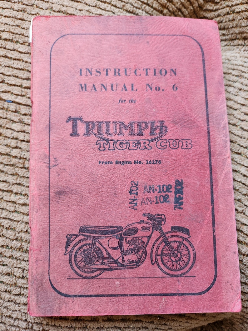 May include: A vintage Triumph Tiger Cub instruction manual. The cover is a faded red with black text and a motorcycle illustration. The text reads "INSTRUCTION MANUAL No. 6" and "TRIUMPH TIGER CUB".