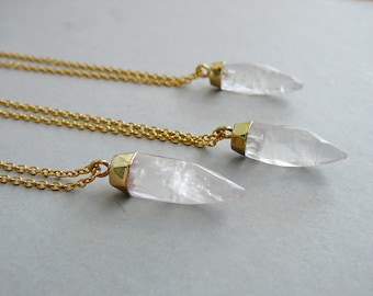 Puede incluir: Tres collares de cadena dorada con colgantes de cristal de cuarzo transparente. Los colgantes son de diferentes tamaños y todos están unidos a las cadenas con cierres dorados.