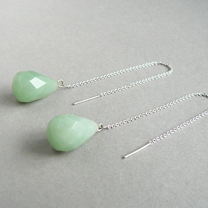 May include: A pair of silver chain earrings with light green gemstone drops. The earrings are dangle style and have a delicate chain.
