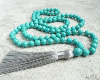 May include: A turquoise blue mala necklace with a silver tassel. The necklace is made of round beads and is strung on a thin cord.