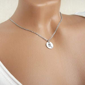 May include: A silver necklace with a round pendant featuring the zodiac symbol for Scorpio.