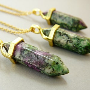 Puede incluir: Tres collares de oro con colgantes de piedra preciosa verde, rosa y blanca. Los colgantes son facetados y tienen una forma puntiaguda.