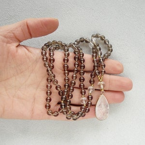 May include: A brown and clear crystal beaded necklace with a rose quartz pendant. The necklace is made with smoky quartz and clear quartz beads.