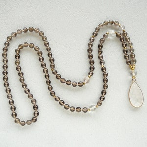 May include: A brown and clear crystal beaded necklace with a large clear crystal pendant. The necklace is made of faceted beads and has a gold accent.