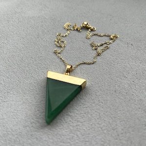 May include: A gold chain necklace with a green triangle pendant. The pendant has a gold trim around the edges.