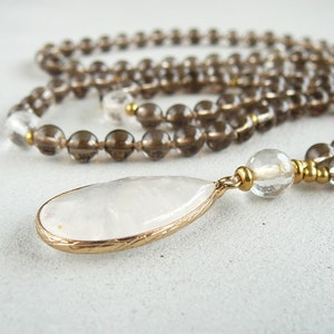 May include: A brown and clear crystal beaded necklace with a large white teardrop pendant. The pendant is set in gold tone metal.
