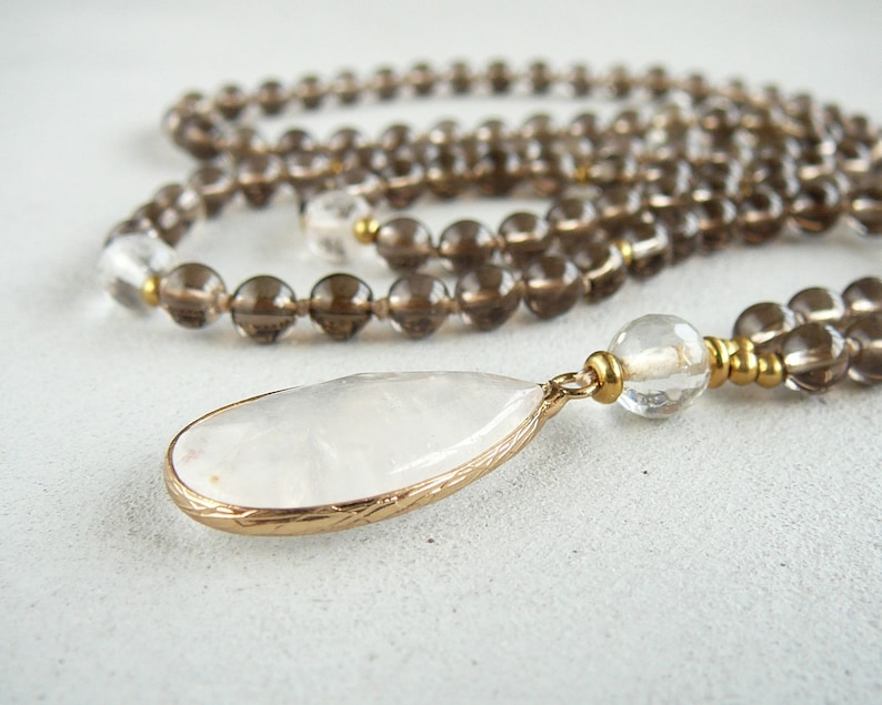 May include: A brown and clear crystal beaded necklace with a large white teardrop pendant. The pendant is set in gold tone metal.