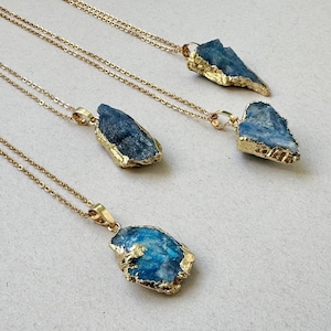 Puede incluir: Tres collares con colgantes de cianita azul en bruto con bordes electroformados en tono dorado. Cada colgante cuelga de una delicada cadena dorada. Las piedras muestran variaciones naturales en forma y color azul profundo, con bordes metálicos dorados texturizados que rodean los bordes irregulares de los cristales.