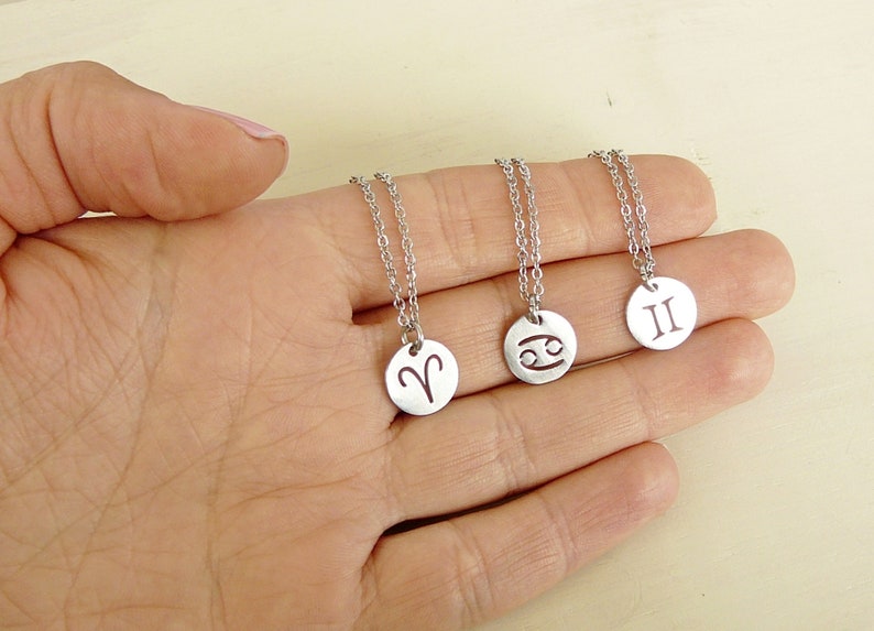Op de afbeelding: Drie zilveren kettingen met sterrenbeeld symbolen. De kettingen hebben een zilveren ketting en een ronde hanger met de sterrenbeeld symbolen voor Ram, Kreeft en Tweelingen.