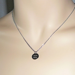 Op de afbeelding: Een zilveren ketting met een ronde hanger met het astrologische symbool voor Waterman.