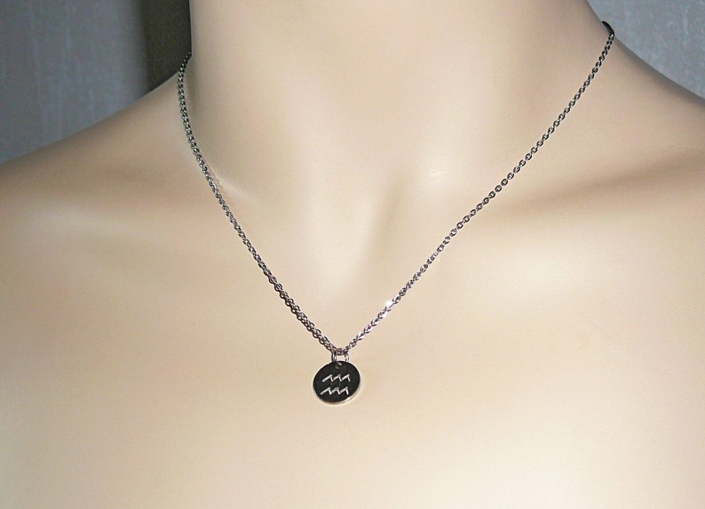 Op de afbeelding: Een zilveren ketting met een ronde hanger met het astrologische symbool voor Waterman.