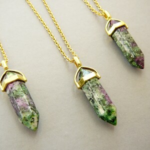 May include: Three gold necklaces with green, pink, and white gemstone pendants. The pendants are shaped like long, pointed crystals.