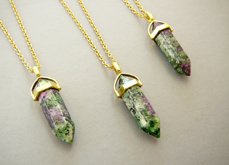 May include: Three gold necklaces with green, pink, and white gemstone pendants. The pendants are shaped like long, pointed crystals.
