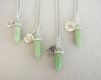 May include: Four silver necklaces with green crystal pendants and different silver charms. The charms include a lotus flower, a tree of life, a hamsa hand, and an om symbol.