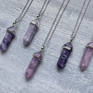 Puede incluir: Cinco collares con colgantes de cristal morado de corte hexagonal puntiagudo suspendidos de cadenas de metal plateado. Cada colgante est&aacute; asegurado con una tapa de metal plateado en la parte superior, mostrando tonos de lavanda y violeta.