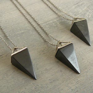 Puede incluir: Tres collares de plata con colgantes en forma de pirámide negra. Los colgantes tienen un borde plateado.