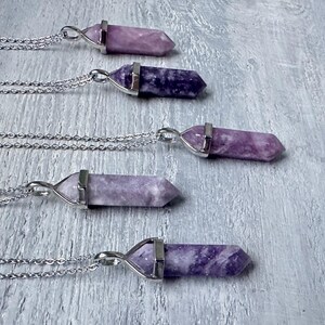 Puede incluir: Cinco collares con colgantes de cristal hexagonal puntiagudos en varios tonos de morado y lavanda. Cada piedra est&aacute; asegurada en una tapa de metal plateado y unida a una delicada cadena plateada, dispuestas en una fila paralela.