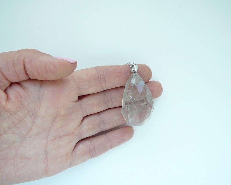 Op de afbeelding: Een heldere kwartskristal hanger aan een zilveren ketting. De hanger is gefacetteerd en heeft een traanvorm.