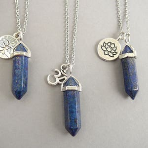 May include: Three silver necklaces with lapis lazuli crystal pendants. The pendants are shaped like a point and have silver caps. Each necklace has a different charm: a tree, a lotus flower, and an Om symbol.