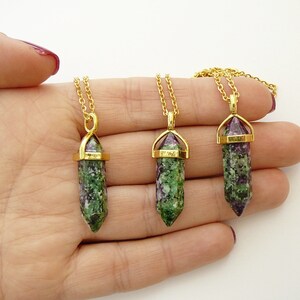 May include: Three gold necklaces with green and purple gemstone pendants. The pendants are shaped like long, pointed crystals with gold caps.