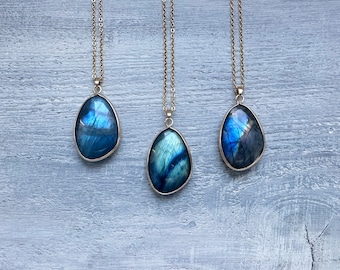 May include: Three gold necklaces with teardrop-shaped labradorite pendants. The pendants are a deep blue with iridescent flashes of green and gold.